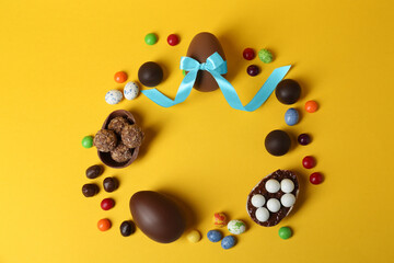 Frame of chocolate eggs and candies on yellow background, flat lay. Space for text