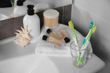 Fototapeta na wymiar Colorful toothbrushes in glass holder and cosmetic products on washbasin