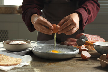 Woman cooking schnitzel at wooden table indoors, closeup