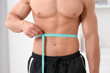 Athletic man measuring waist with tape at home, closeup. Weight loss concept