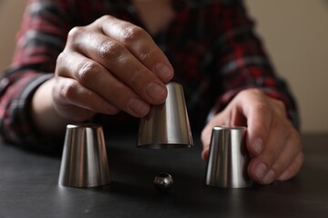 Woman playing thimblerig game with cups and metal ball at black table, closeup