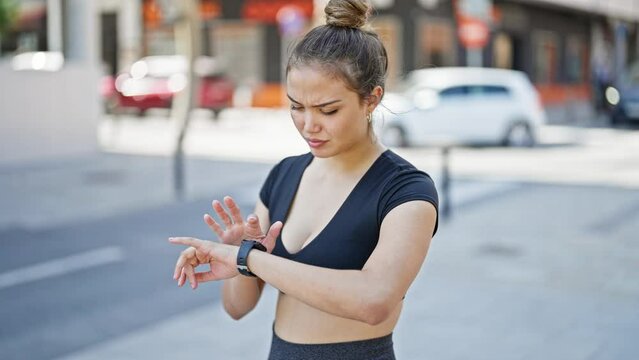 Young beautiful hispanic woman wearing sportswear using smartwatch at street