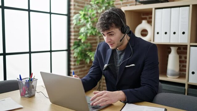 Young hispanic man business worker using laptop wearing headset at office