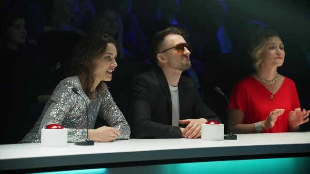 Portrait of celebrity judges enjoying the audition performed by talent on stage during the recording of a broadcast TV television talent show 