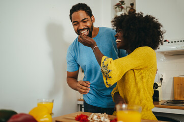 A happy african american couple is cooking dinner together and eating organic vegetables in the...