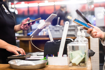Fototapeta premium Selective focus to edge of smartphone in hand with blurry the tablet and cashier staff using it to receive orders from customers at counter service in cafe or store.