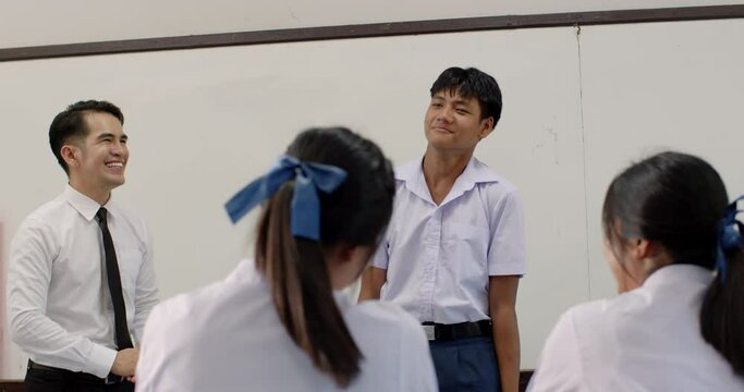 Asian high school classroom with a smiling male teacher teaching English with young girls and boy in white school uniforms and students studying actively and having fun teaching activities.