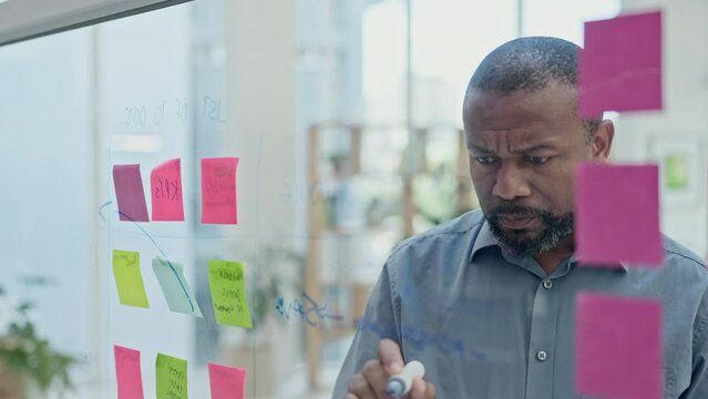 Business, black man and writing on glass with focus for planning, ideas and problem solving in office. Serious, mature male worker and brainstorming timeline, solution and mindmap process at window
