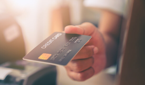 Customer holding credit card for payment on card reader machine to owner at restaurant.