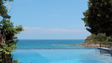 Stunning view from infinity swimming pool overlooking turquoise sea. Relaxation and luxury at a beachside resort with beautiful nature and clear blue skies. Concept of travel and summer vacation.