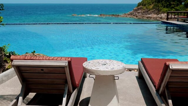 Two beach chairs and a cocktail table near a swimming pool on a sunny day. Summer vacation. Concept of relaxation and leisure.