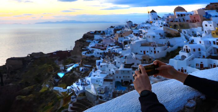 Young tourist man hand using smartphone take picture at View of blue church dome in Oia village,Santorini,Greece