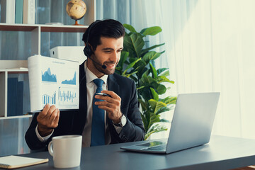 Business man wearing headphone present financial data or BI paper via laptop during online meeting....