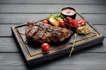 Hot grilled pork steak from a summer BBQ served with a hot chili pepper and cherry tomatoes on an old wooden cutting board.