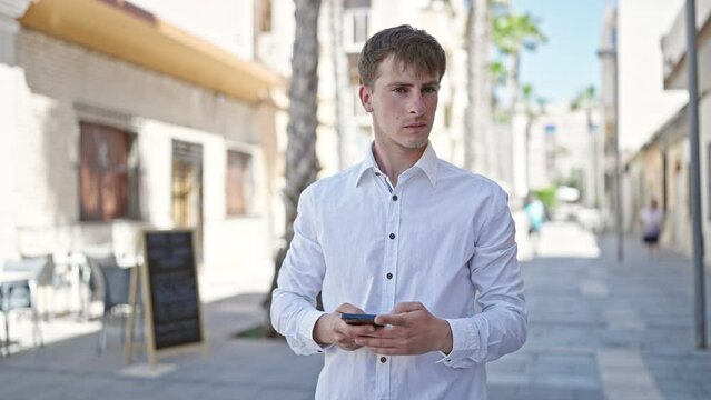 Young caucasian man using smartphone with serious expression at street