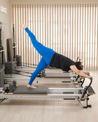 Overweight caucasian woman doing pilates exercises on a reformer. 