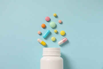 Various medicines and health pills poured from a medical white bottle, healthcare and medical on a colorful blue background