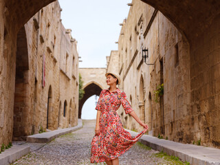 summer trip to Rhodes island, Greece. Young Asian woman in ethnic red dress walks Street of Knights of Fortifications castle. female traveler visiting southern Europe. Unesco world heritage site.