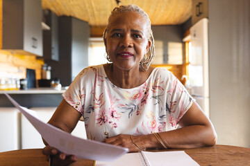 Happy senior african american woman holding documents, making video call at home