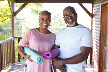 Portrait of happy senior african american couple holding yoga exercise mats on terrace