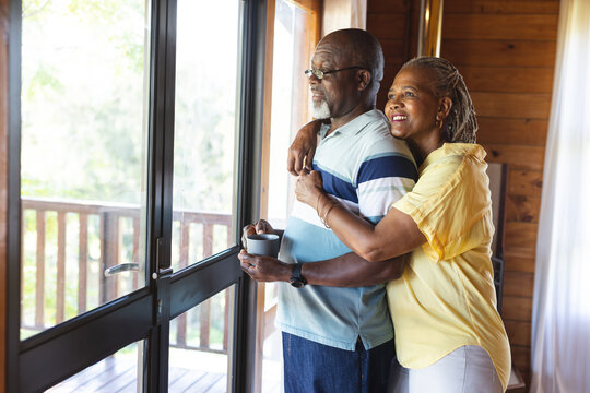 Happy senior african american couple embracing and looking out window at home, copy space