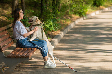 Obraz premium Blind young woman cuddling with guide dog while sitting on a bench. 