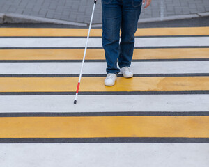 Close-up of the legs of a blind woman crossing the road at a crosswalk with a cane. 