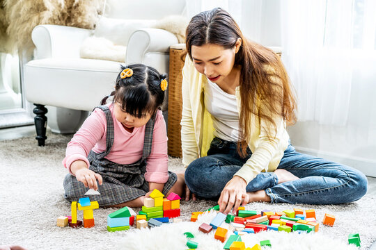 Young asian mother and little daughter enjoy to play puzzle wood toy together in area of living room of their house and they look happiness, childhood and motherhood concept