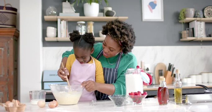 Happy african american mother and daughter preparing dough in bowl in kitchen, slow motion