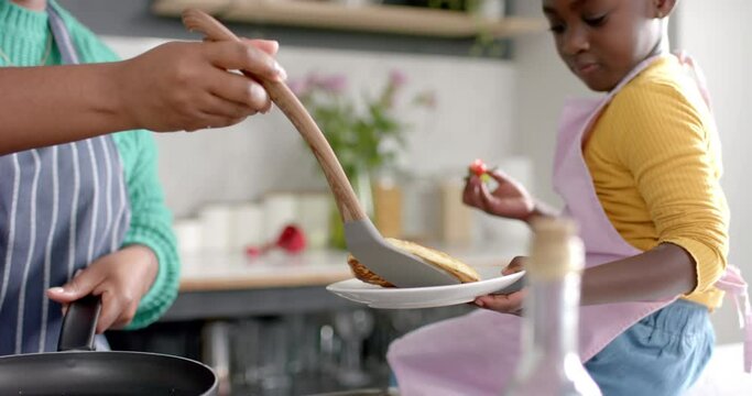 Happy african american mother and daughter preparing pancakes in kitchen, slow motion