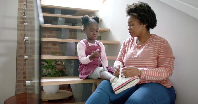 African american mother advising and tying shoes of daughter at home, slow motion