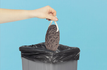 Throw pumice stone in trash can, volcanic pumice stone in hand in front of trash can, gray trash...