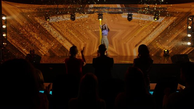 Judges press the golden buzzer to send a contestant to a show finale, the lights changing to gold, young woman dancer talent is happily surprised. Television style broadcast talent show