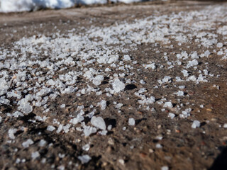Macro shot of big, white salt grains on icy sidewalk surface in the winter. Applying salt to pathways to keep surface clear and people safe in winter weather from ice or snow
