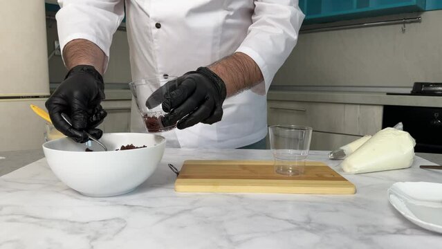 The process of making a trifle cake in transparent cups, creating confectionery sweets and desserts. Close-up. Hands in black gloves make a trifle cake.