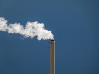 View of a huge metal chimney with white and grey dense smoke from burning firewood, pellets or briquettes