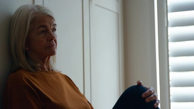 Handheld shot of unhappy senior woman suffering with mental health problems sitting on floor of room at home alone - shot in slow motion