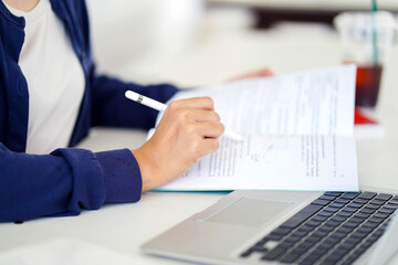 Closeup and crop young female student in casual cloth reading a book with laptop for the exam on blurred background.
