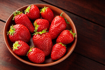 Fresh ripe delicious strawberries in clay plate on wooden background. Close up