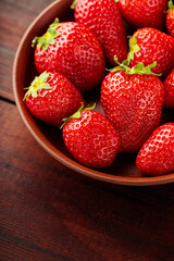 Fresh ripe delicious strawberries in clay plate on wooden background. Close up