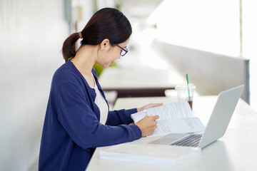 Closeup Asian young female student in casual cloth reading a textbook for the exam with laptop at school building and blurred background. Asian school concept.