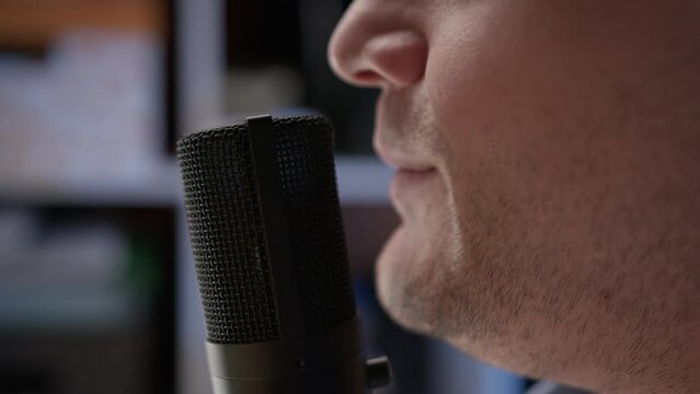 close up view of mouth of unrecognizable young radio host in headphones who sits in recording studio in blue shirt and recites text into microphone. Man record text voice-over. Blogger hosts podcast.