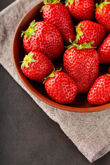 Ripe strawberries in clay plate on dark background. Top view. Copy space