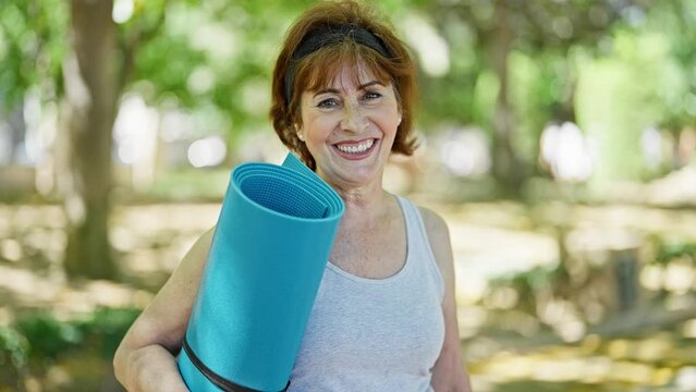 Middle age woman wearing sportswear holding yoga mat at park