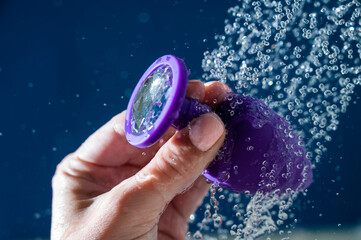 Woman washing purple anal plug under shower on blue background. 
