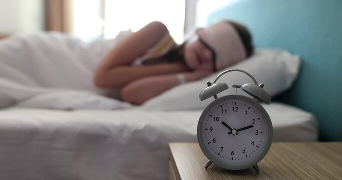 Alarm clock for 10 o'clock on table in children bedroom. Child sleeping soundly in mask in bedroom