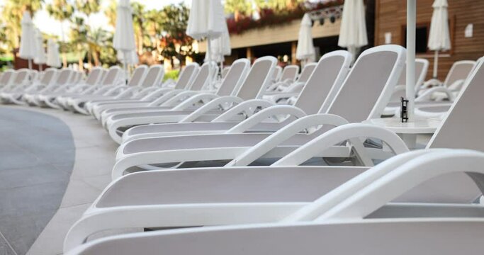 Row of stylish bright sun loungers and umbrellas by pool. Comfortable rest for tourists