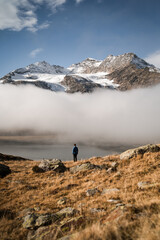 A hiker is enjoying the scenic view of the snowy peaks of the Bernina Pass and Lago Bianco, during an autumnal morning, Switzerland