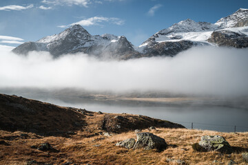The snowy peaks of Mount Bernina appear from the low clouds above the Lago Bianco