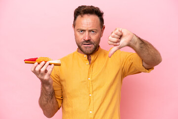 Middle age Caucasian man holding sashimi isolated on pink background showing thumb down with...